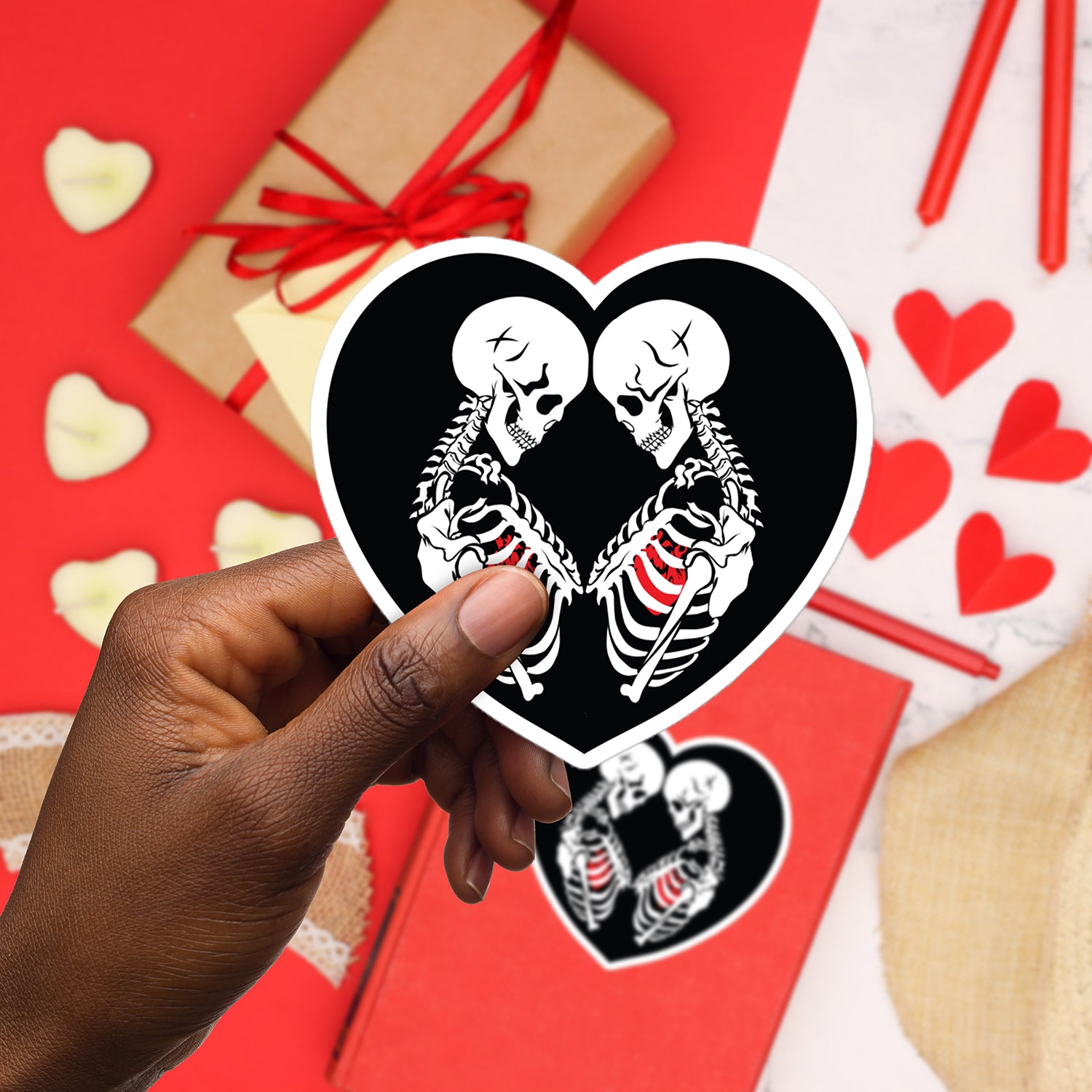 a person holding a heart shaped sticker with two skeletons on it