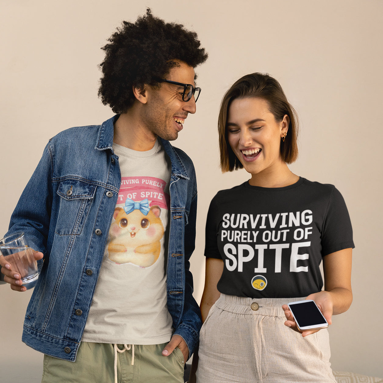 A man and a woman are standing next to each other, smiling and holding drinks. The man is wearing a denim jacket and a t-shirt with a cartoon character, while the woman is wearing a black t-shirt with the text "Surviving purely out of Spite".