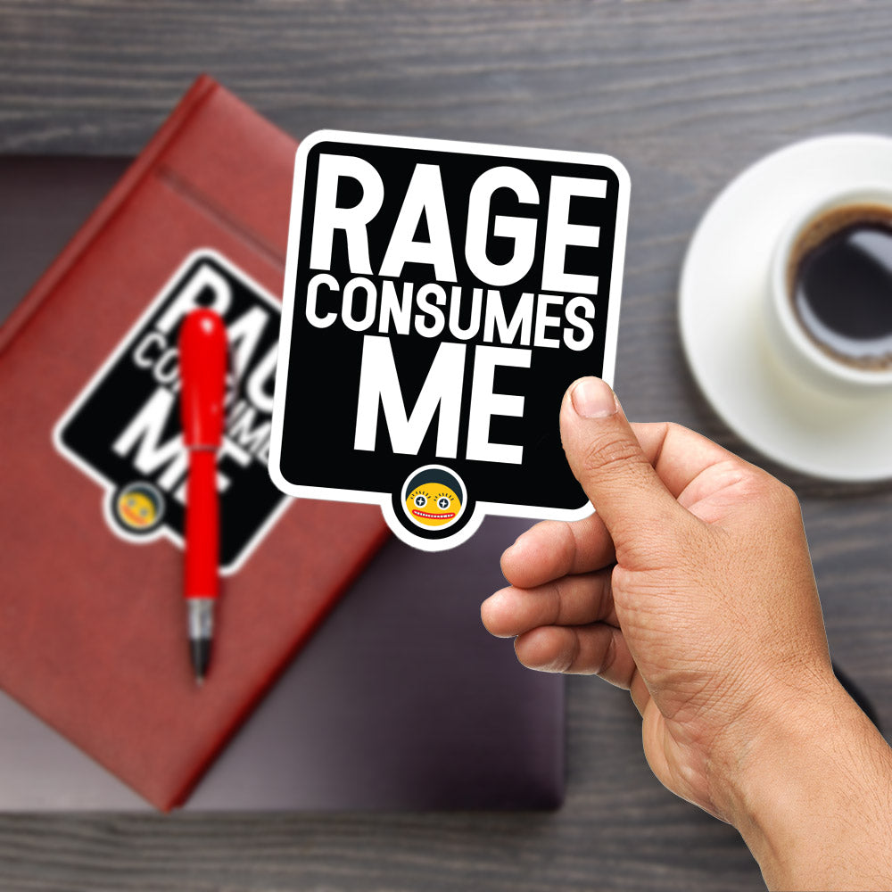A person's hand is holding a sticker with the text "RAGE CONSUMES ME" on a wooden surface, with a red pen and a cup of coffee in the background.