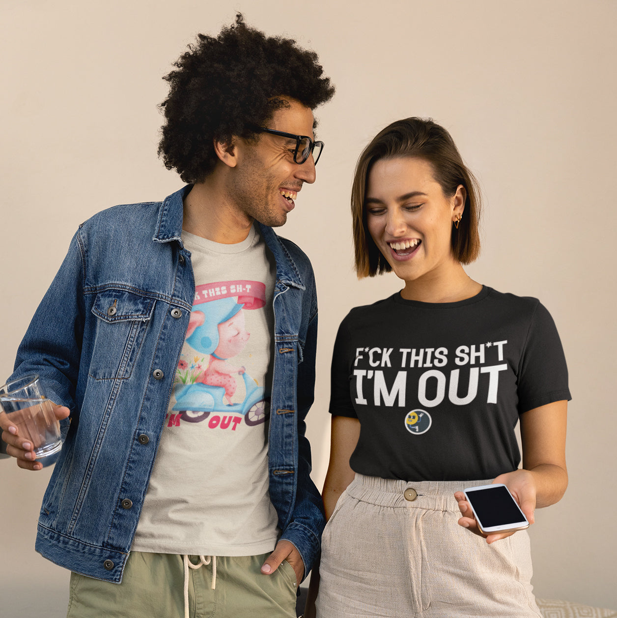 A man and a woman are standing next to each other, smiling and holding drinks. The man is wearing a denim jacket and glasses, while the woman is wearing a black t-shirt with white text.