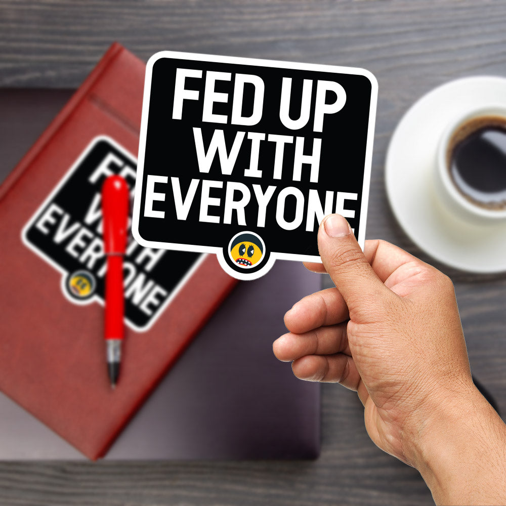 A hand holding a sign with the text "FED UP WITH EVERYONE" is shown in the foreground, with a red pen and a laptop visible in the background.