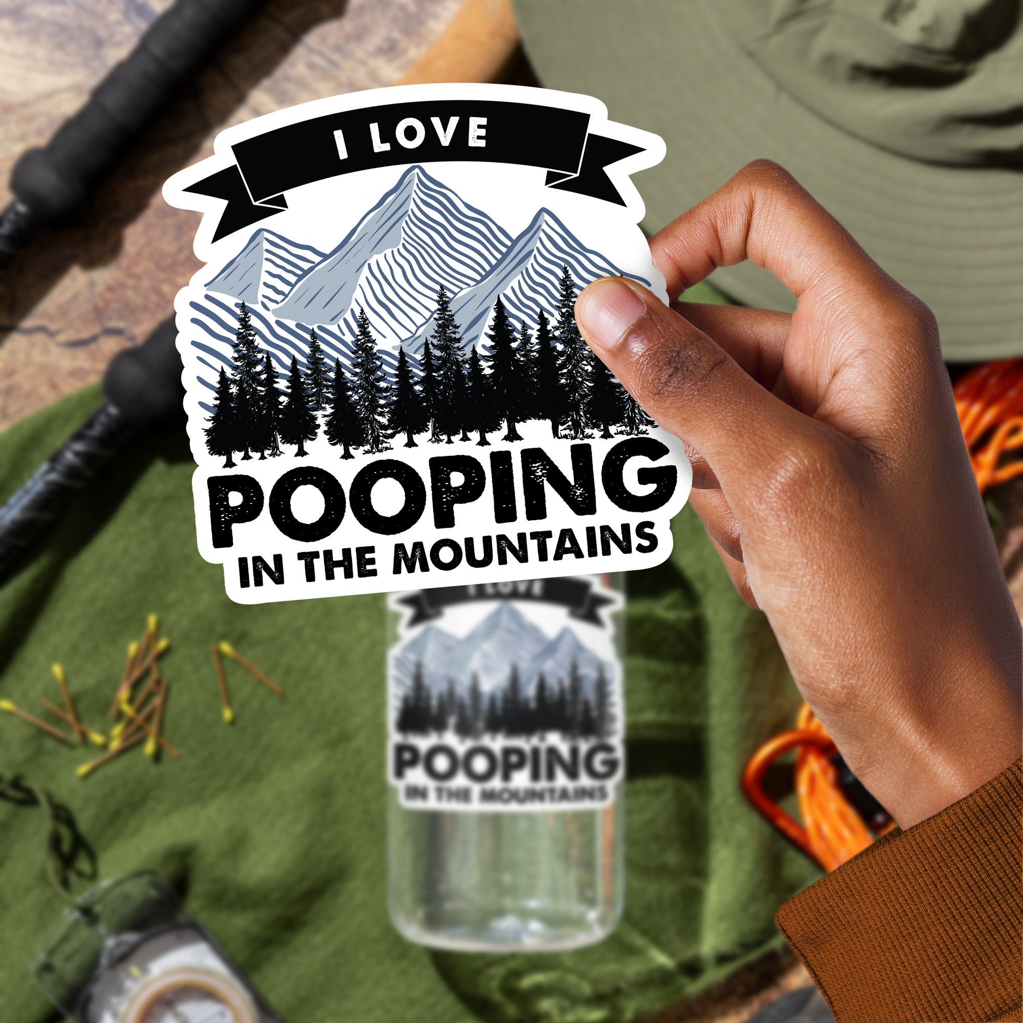 a person holding a sticker that says i love pooping in the mountains