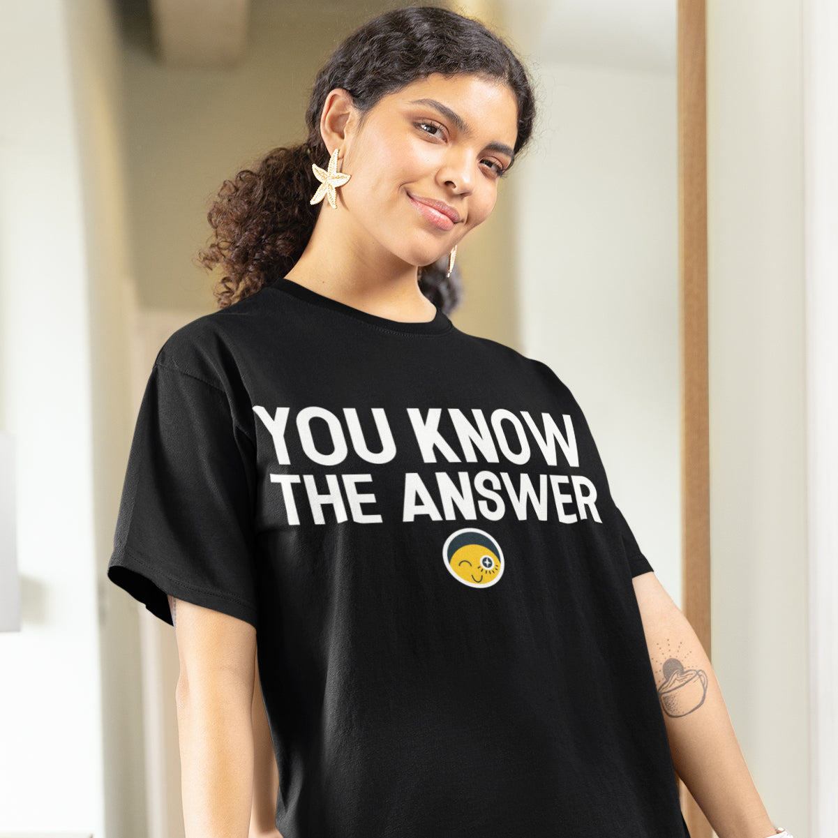 A woman wearing a black t-shirt with the text "YOU KNOW THE ANSWER" and a smile on her face.