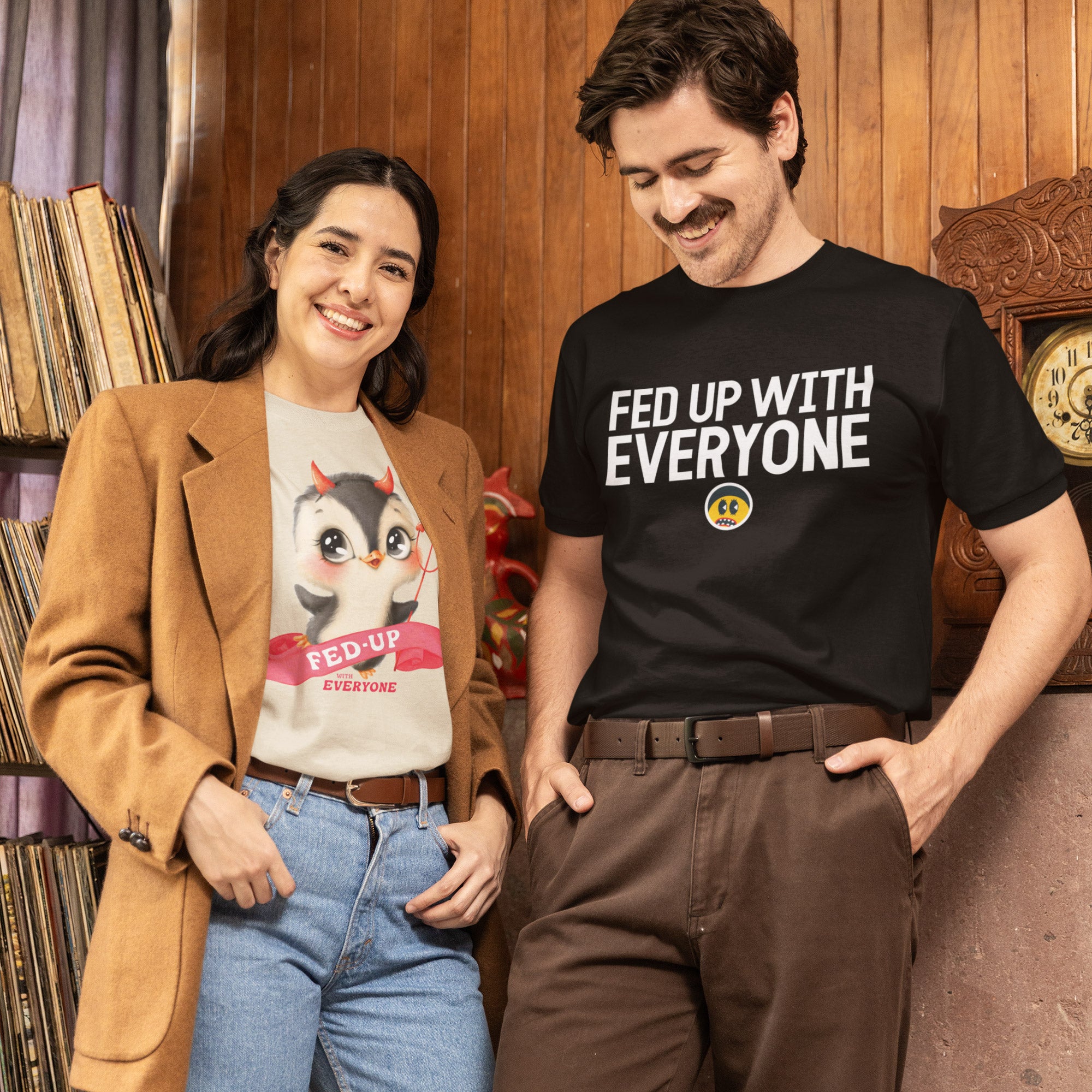 A man and a woman are standing together, smiling and posing for a photo. The man is wearing a black t-shirt with the text "FED UP WITH EVERYONE" printed on it, while the woman is wearing a t-shirt with a cartoon character and the text "FED UP EVERYONE" printed on it.