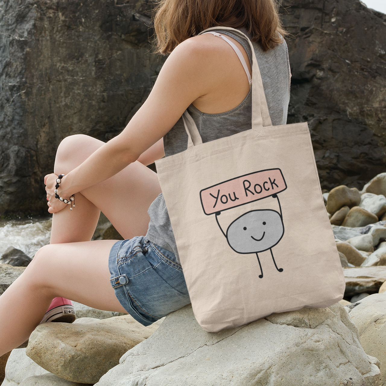 a woman sitting on a rock with a tote bag