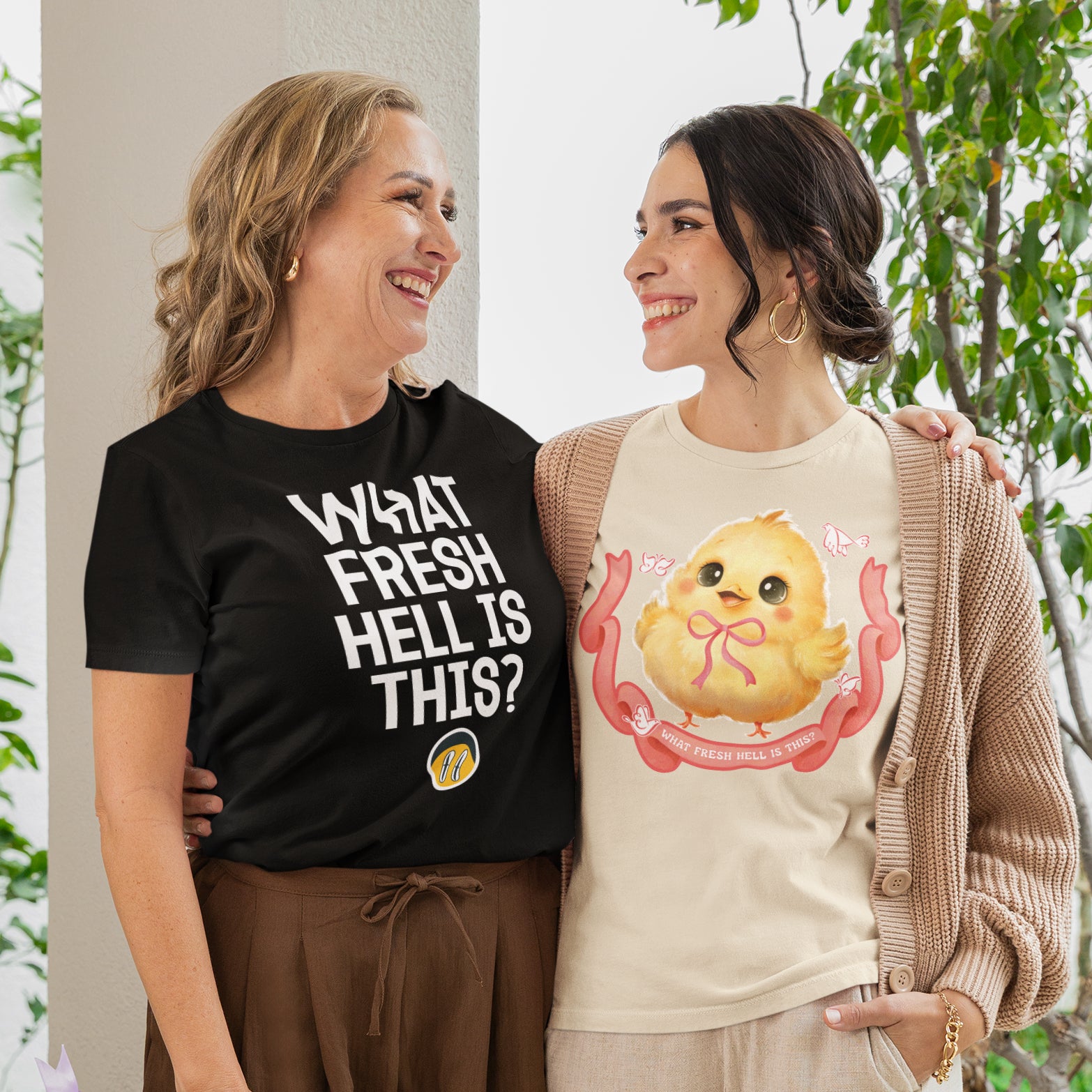 Two women standing together, smiling and posing for a photo. One woman is wearing a black t-shirt with a humorous text, while the other is wearing a t-shirt with a cute cartoon chicken design.