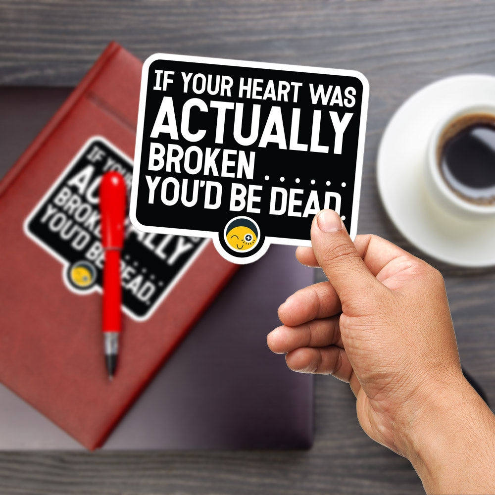 A person's hand holding a sticker with a humorous message, while a red pen and a book are visible in the background.