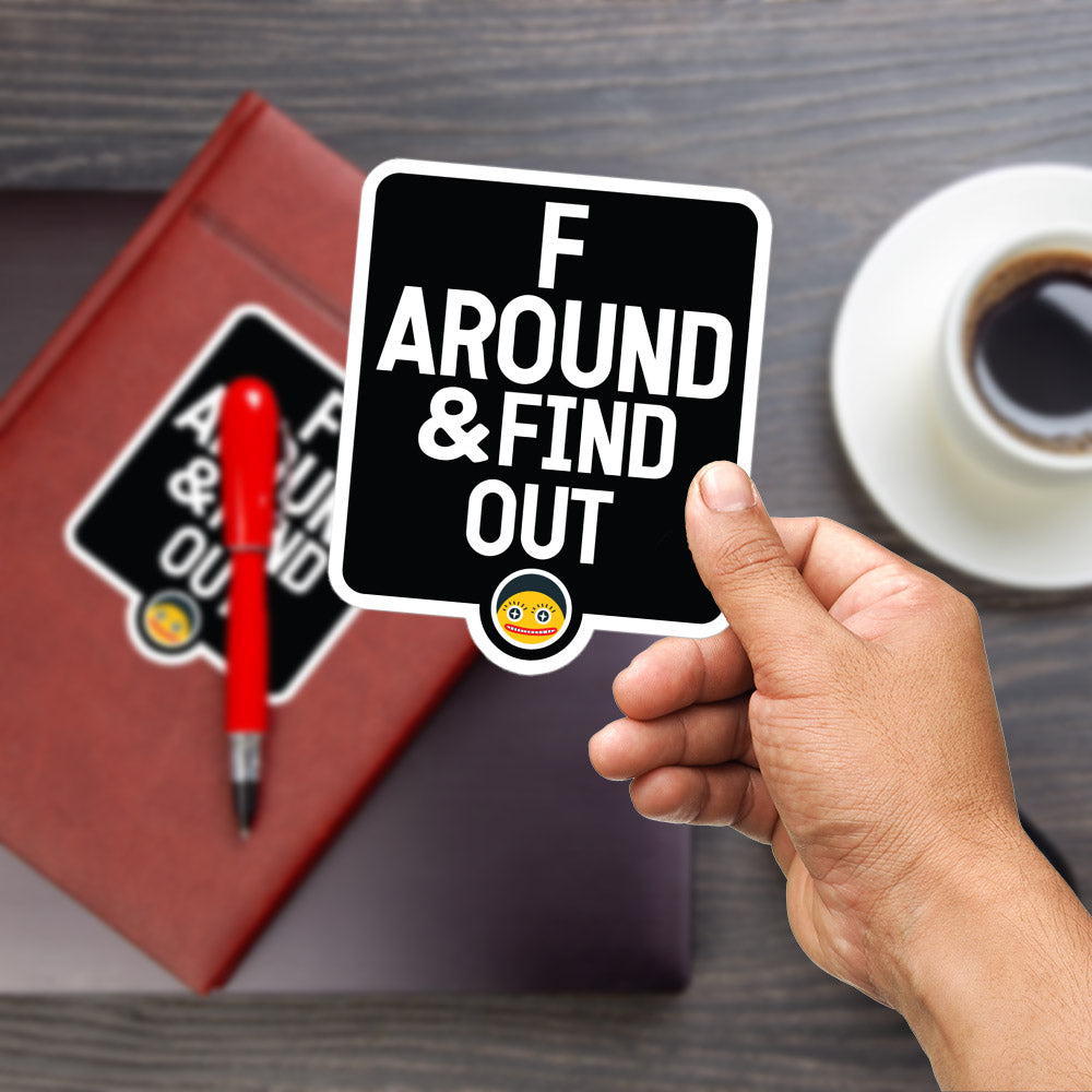 A hand holding a sticker with the text "F AROUND & FIND OUT" is shown in the foreground, with a red pen and a laptop visible in the background.