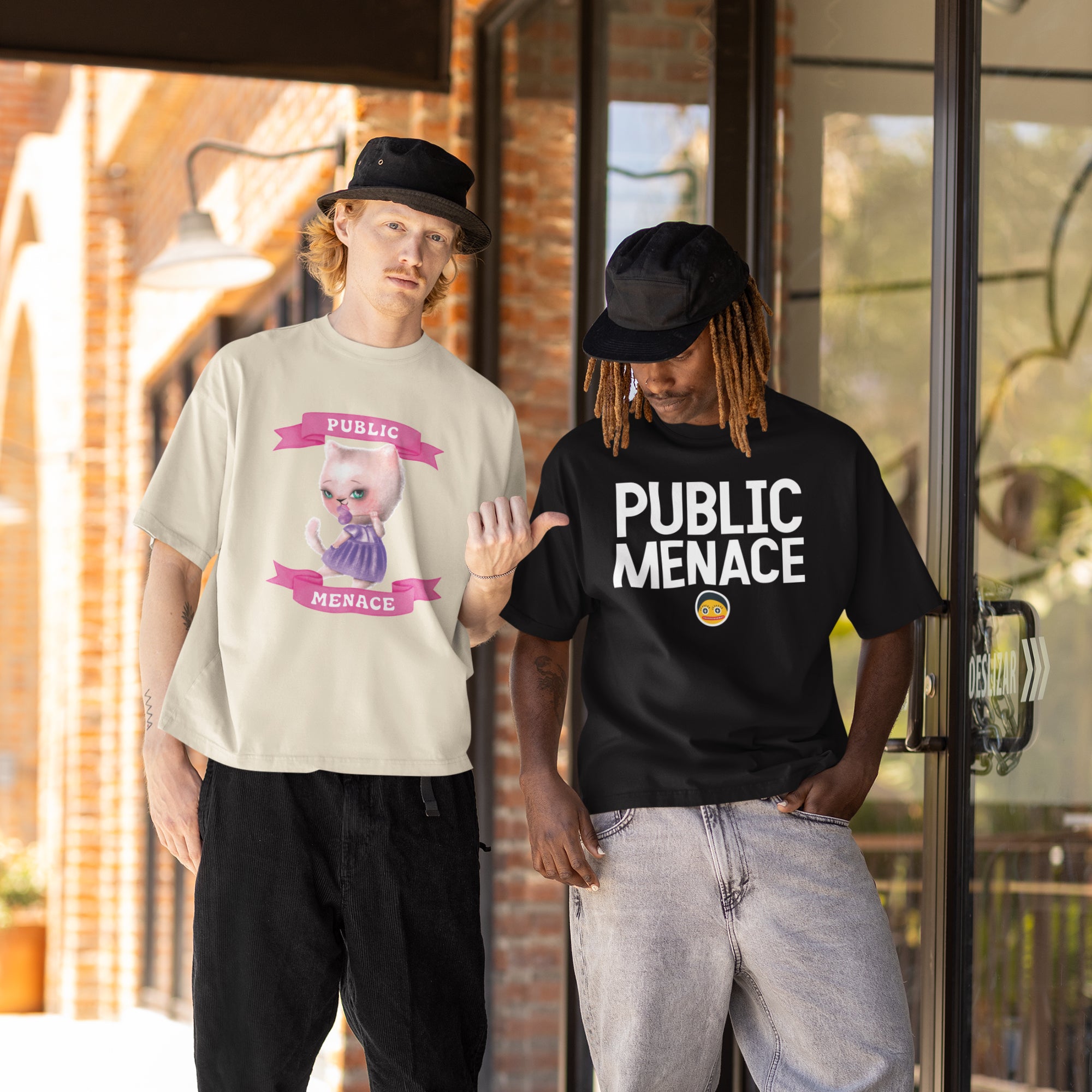 Two men standing outside a building, one wearing a white t-shirt with a cat graphic and the other wearing a black t-shirt with the text "PUBLIC MENACE" printed on it.
