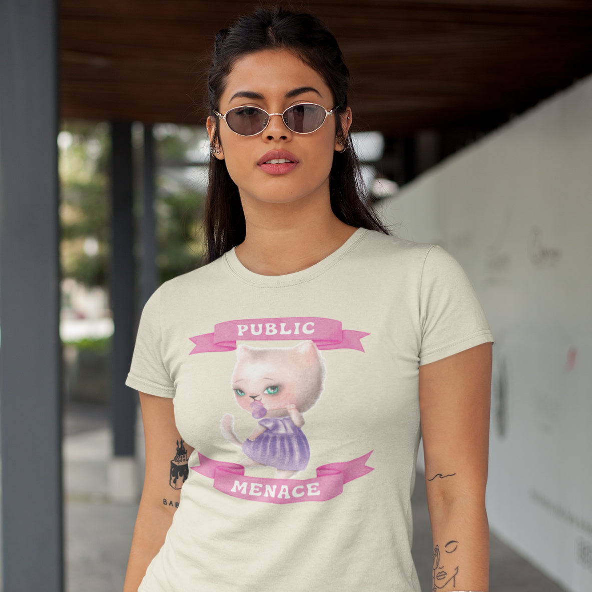 A woman wearing a white t-shirt with a graphic design of a cat and the text "PUBLIC MENACE" printed on it.