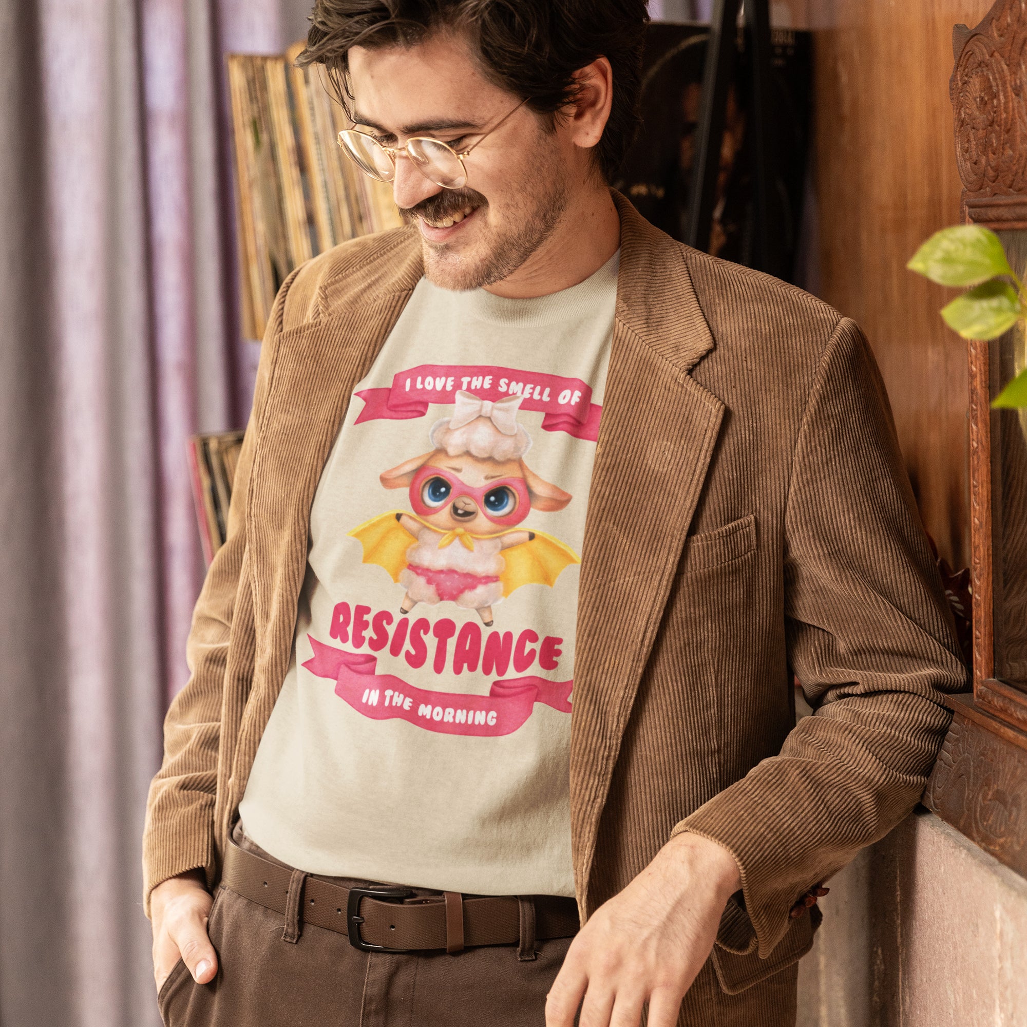 A man wearing a brown jacket and a t-shirt with a cartoon character is leaning against a wall.