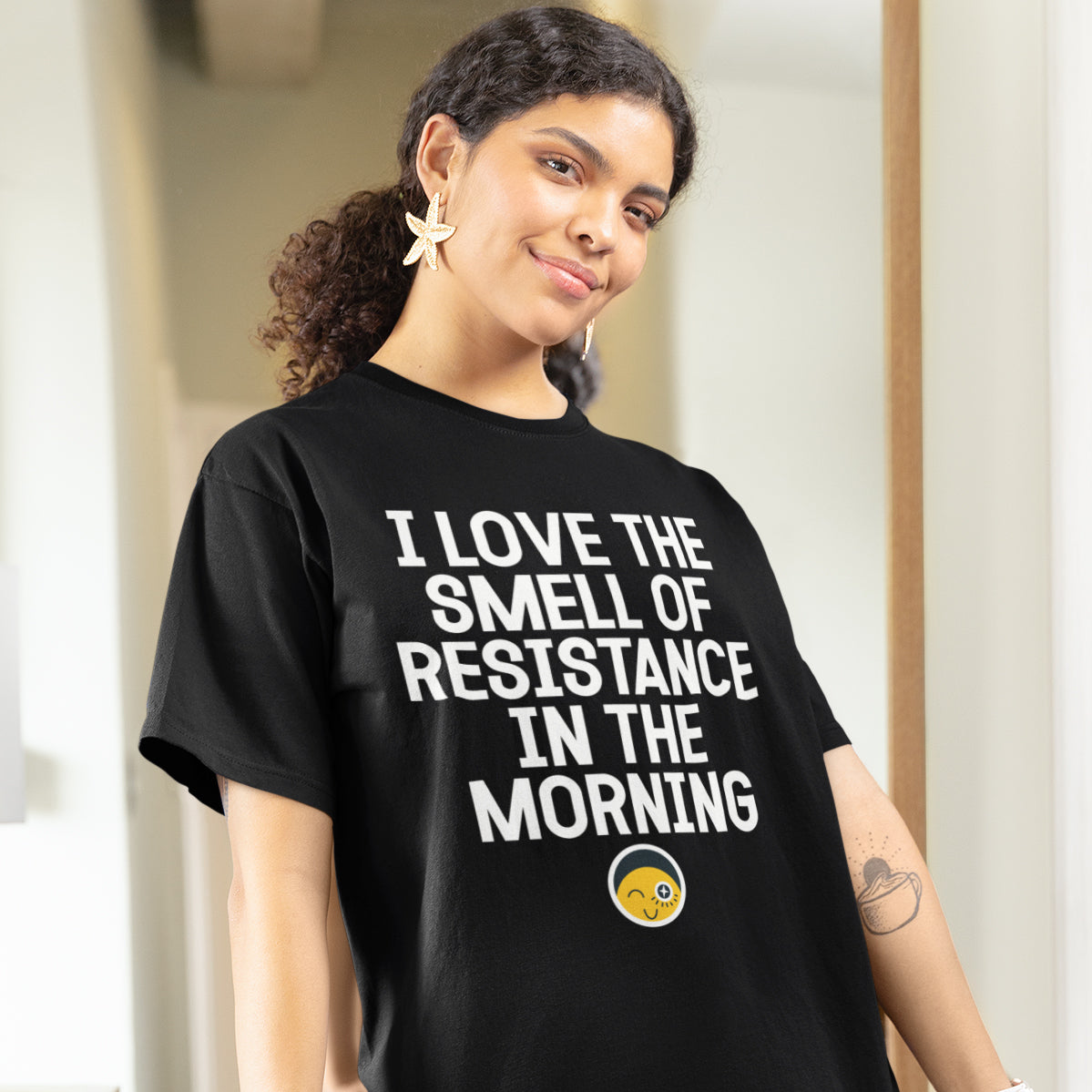 A woman wearing a black t-shirt with white text and a yellow smiley face graphic, smiling at the camera.