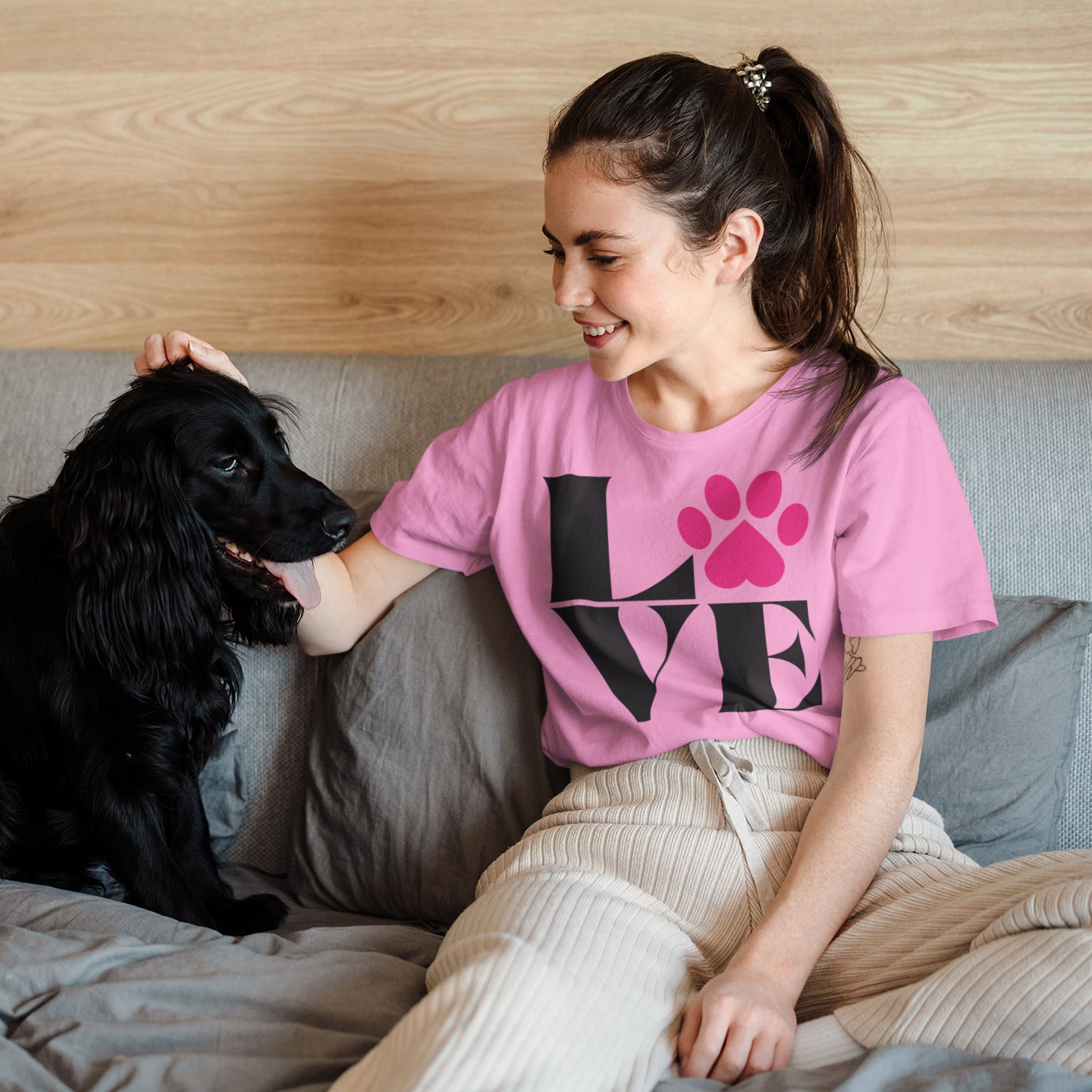 a woman sitting on a bed petting a black dog