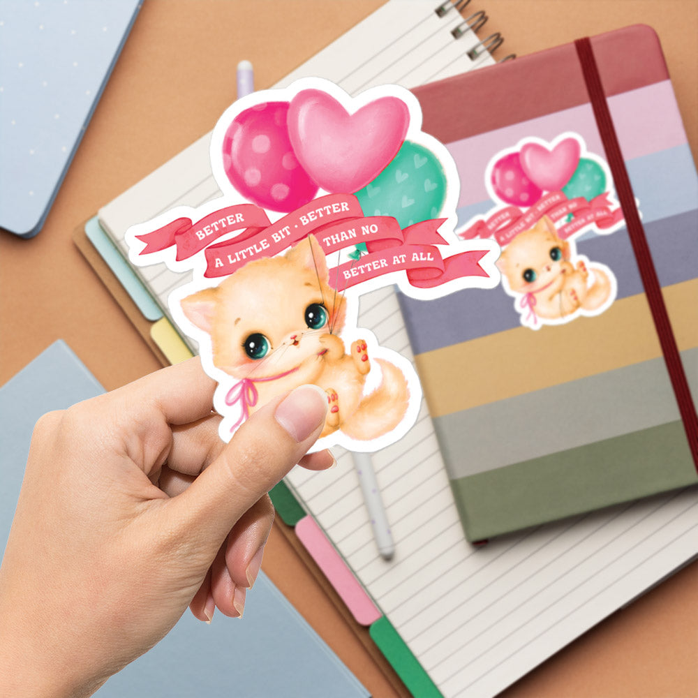 A hand holding a sticker with a cute cartoon cat and heart-shaped balloons.
