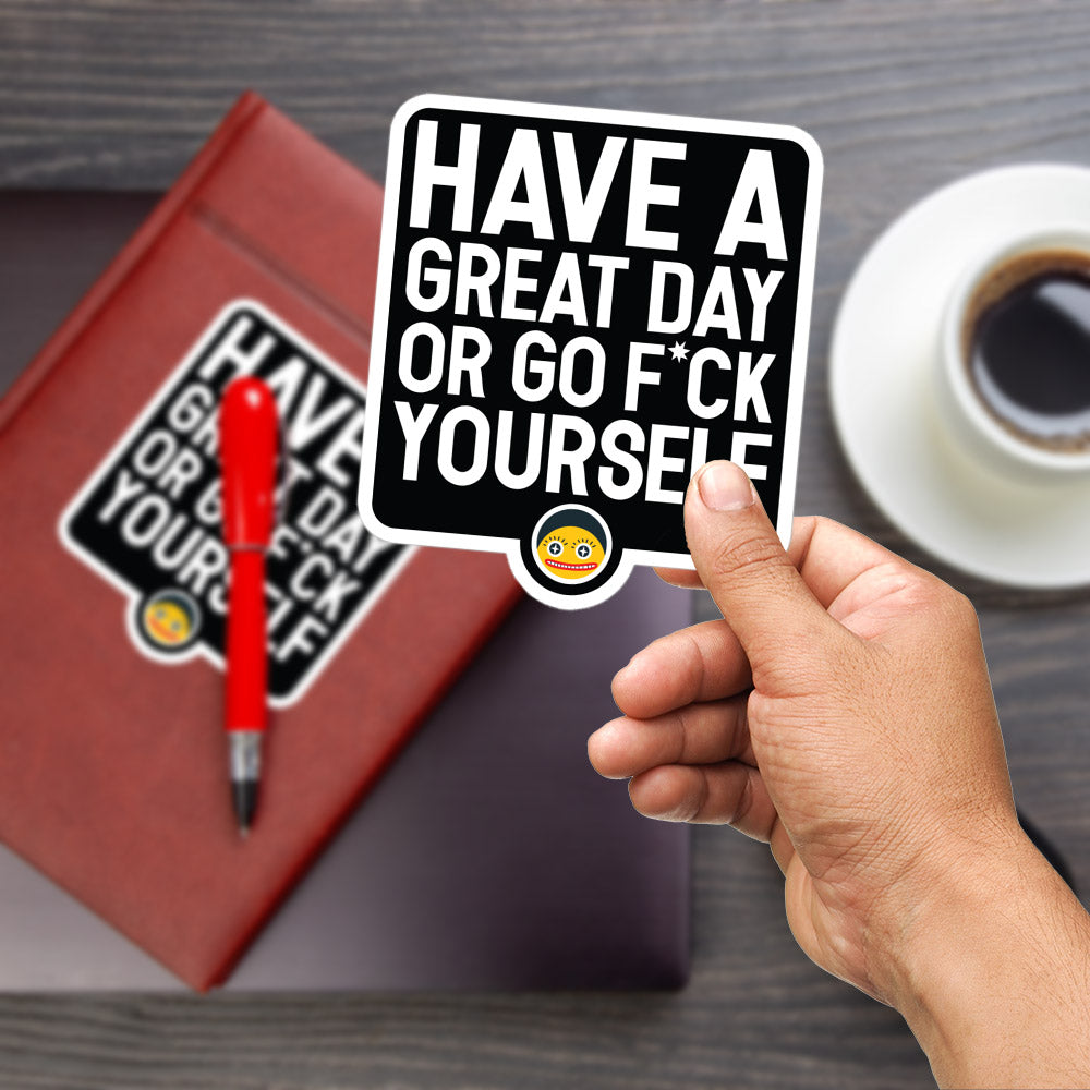 A person's hand is holding a sticker with the text "HAVE A GREAT DAY OR GO F*CK YOURSELF" and a small smiley face sticker. The hand is also holding a red pen and a cup of coffee, suggesting a casual, relaxed setting.