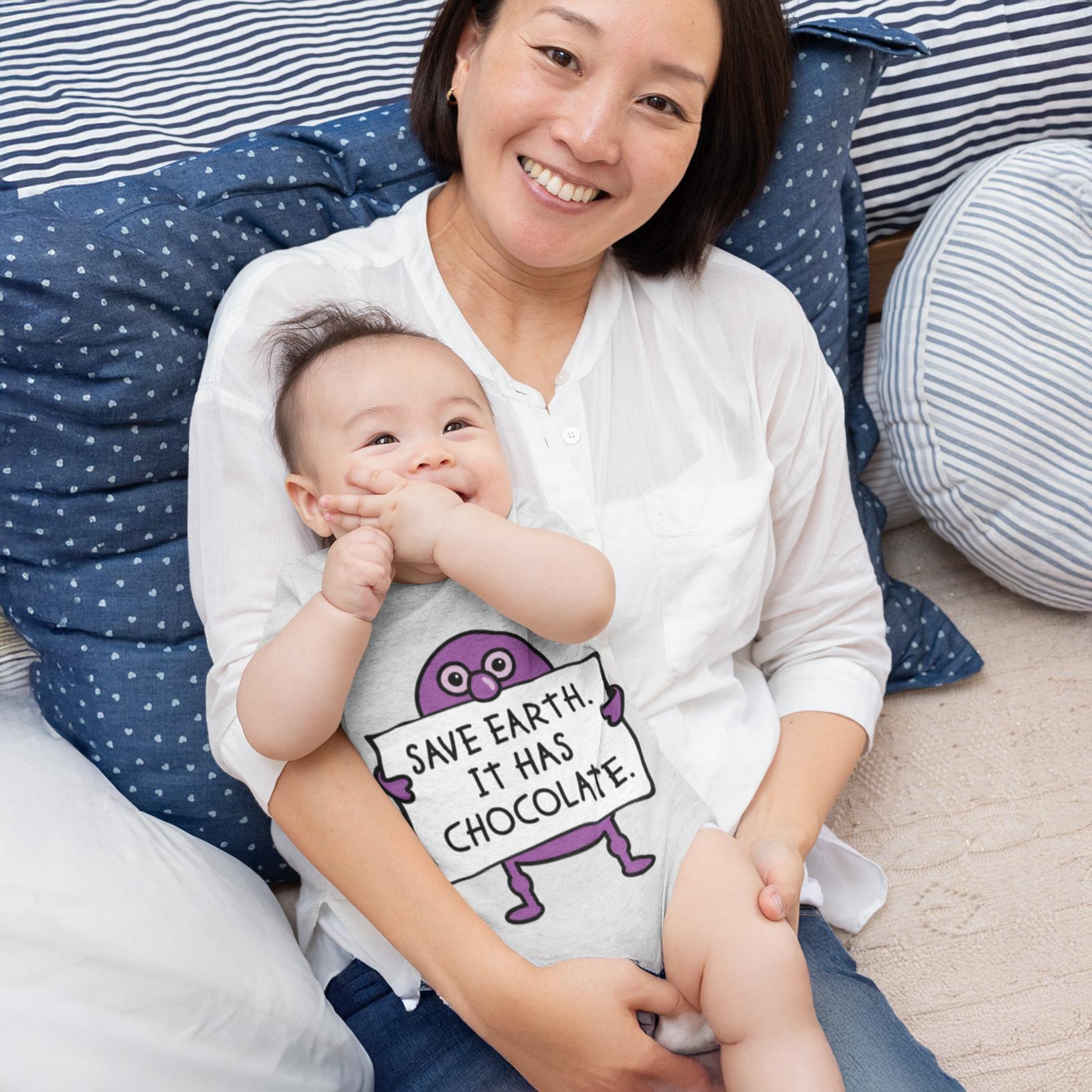 A smiling woman holding a baby in her arms, with the baby wearing a shirt with a cartoon character and text printed on it.