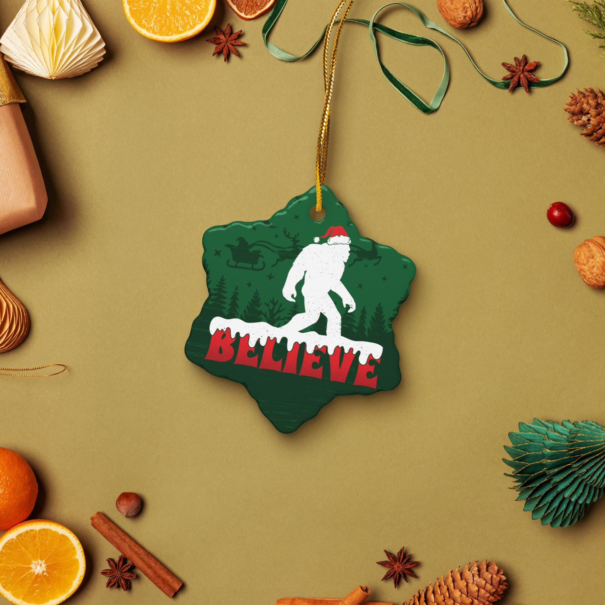 A Christmas ornament with a green star shape and a white Sasquatch silhouette, along with the word "Believe" written on it, is displayed among various holiday decorations and fruits.