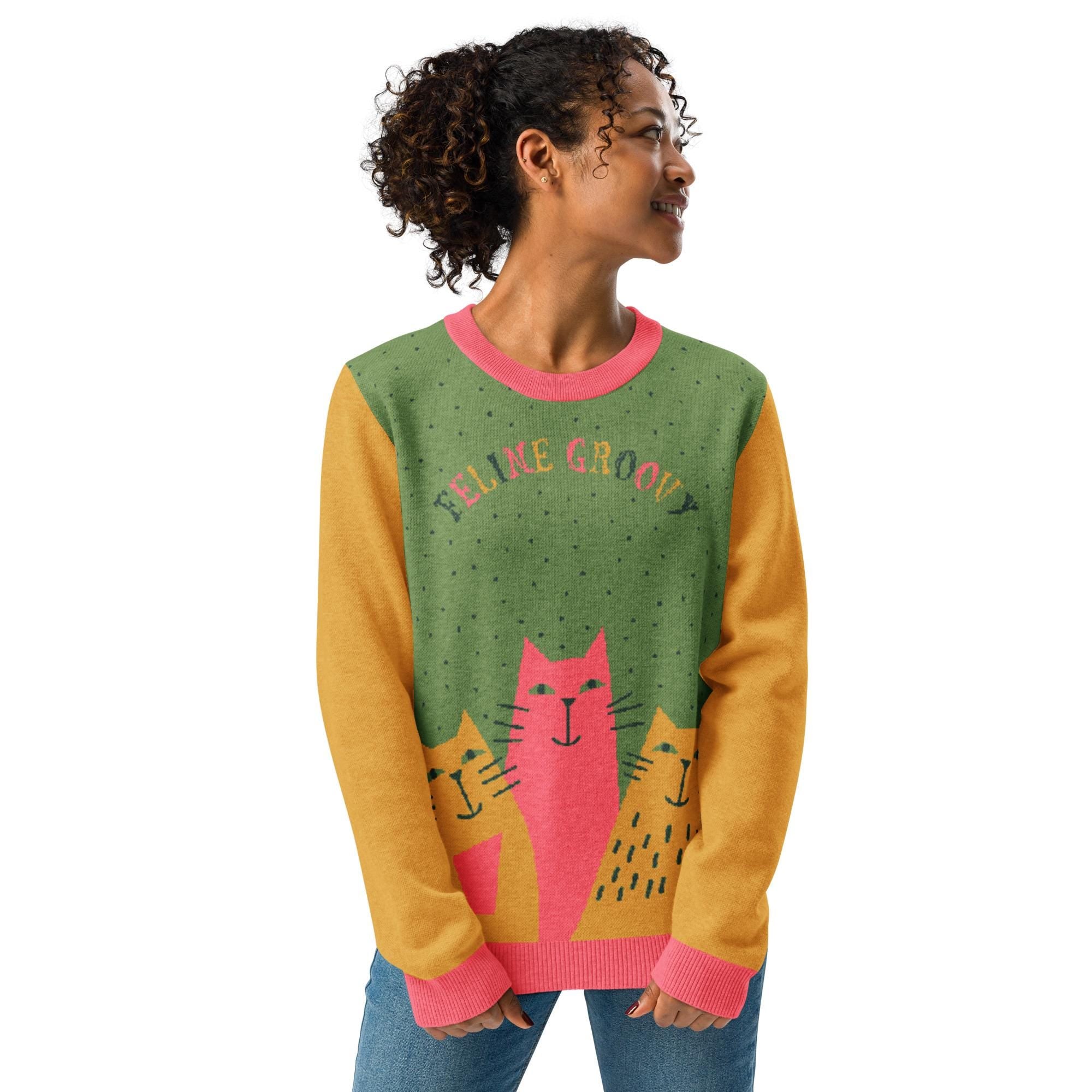 A woman wearing a sweater with a cat design and the text "FELINE GROOVE" printed on it.