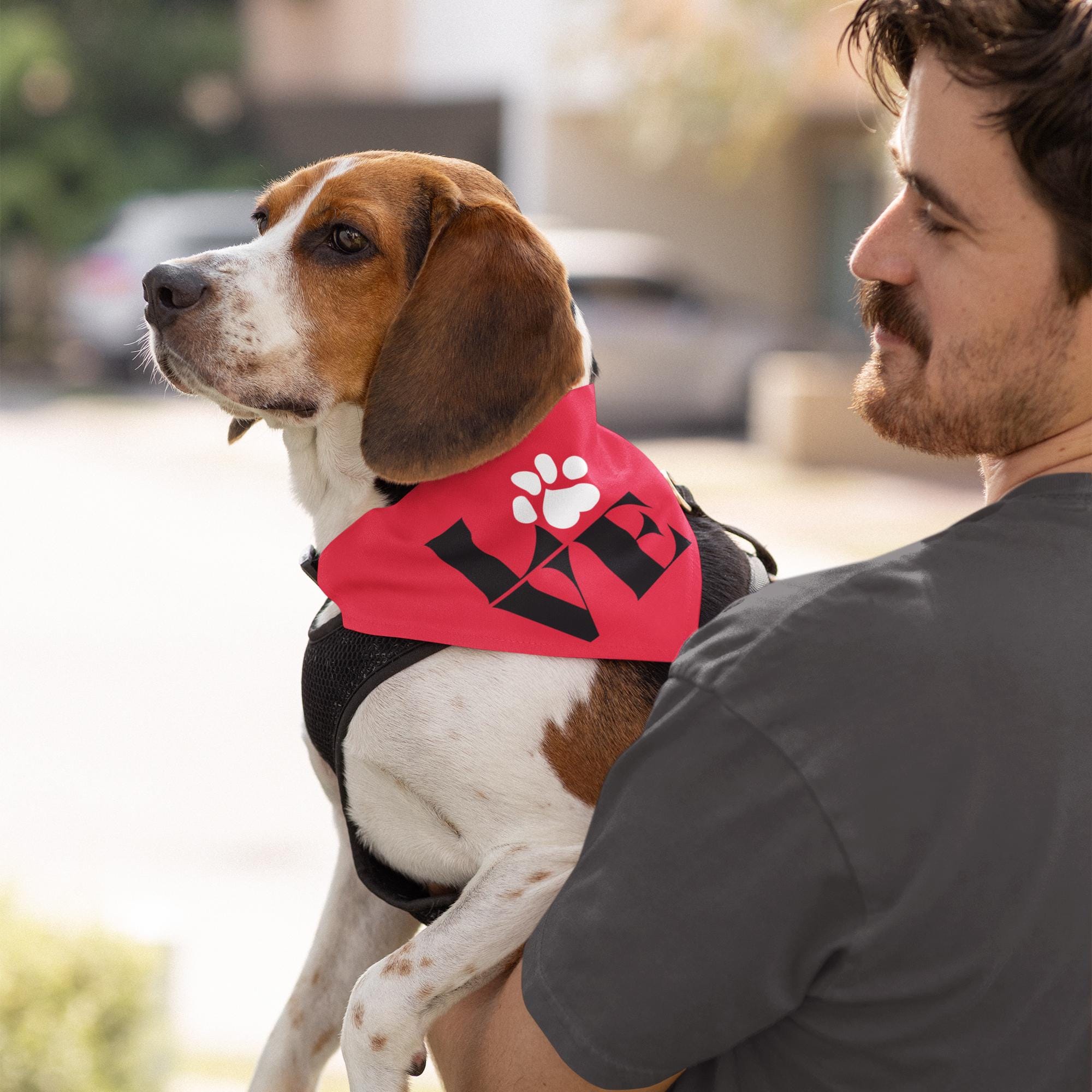 A man is holding a beagle dog wearing a red bandana with the word "LOVE" printed on it.