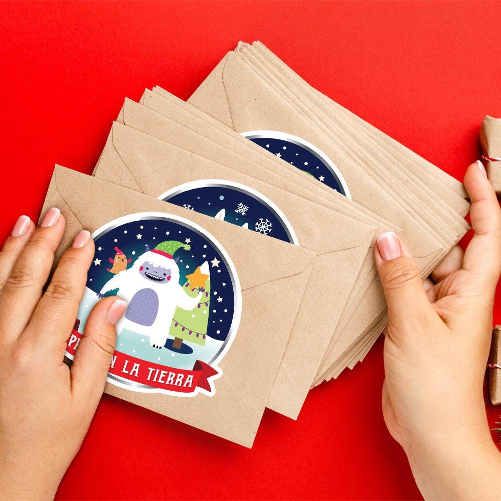 A pair of hands holding a stack of brown envelopes with a festive holiday-themed sticker on them, against a red background.