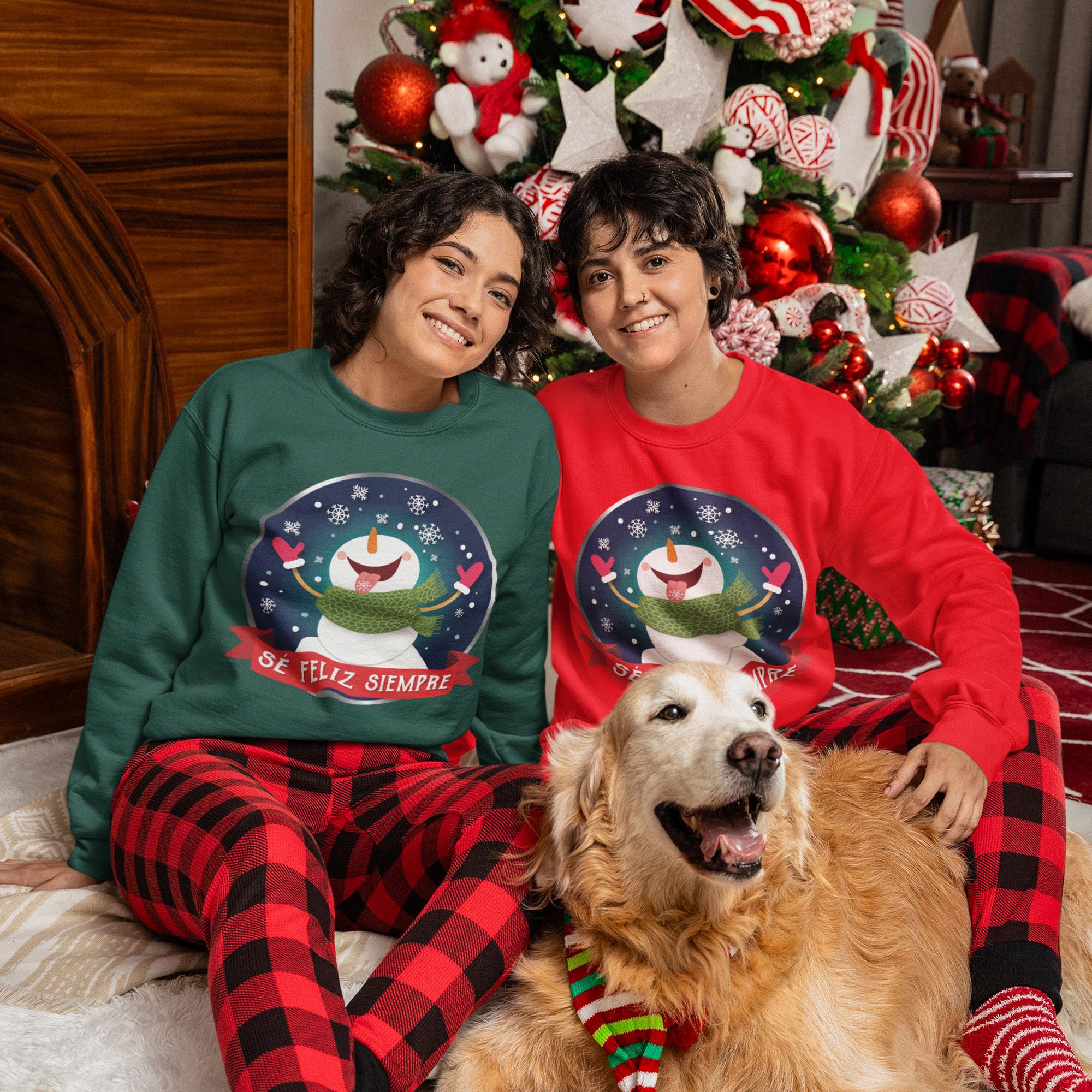 Two people wearing matching Christmas sweaters sit on the floor with a dog in front of a decorated Christmas tree.