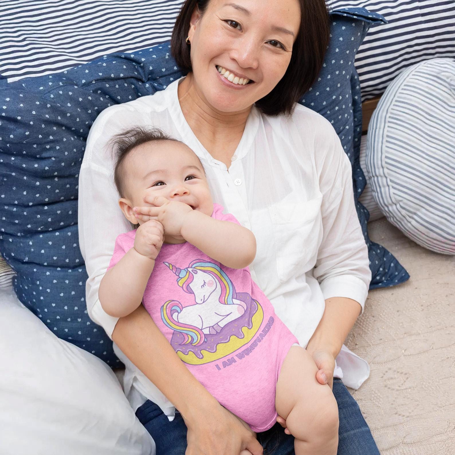 A smiling woman holding a baby in a cozy setting with blue and white pillows.