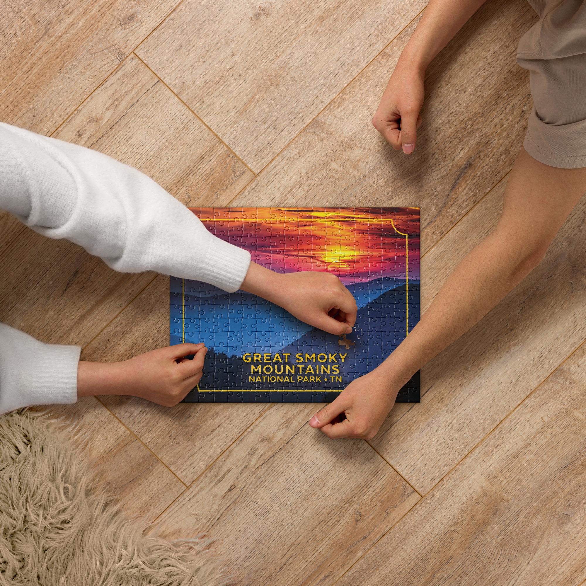 Two people are working together to assemble a puzzle depicting a scenic mountain landscape with a sunset.