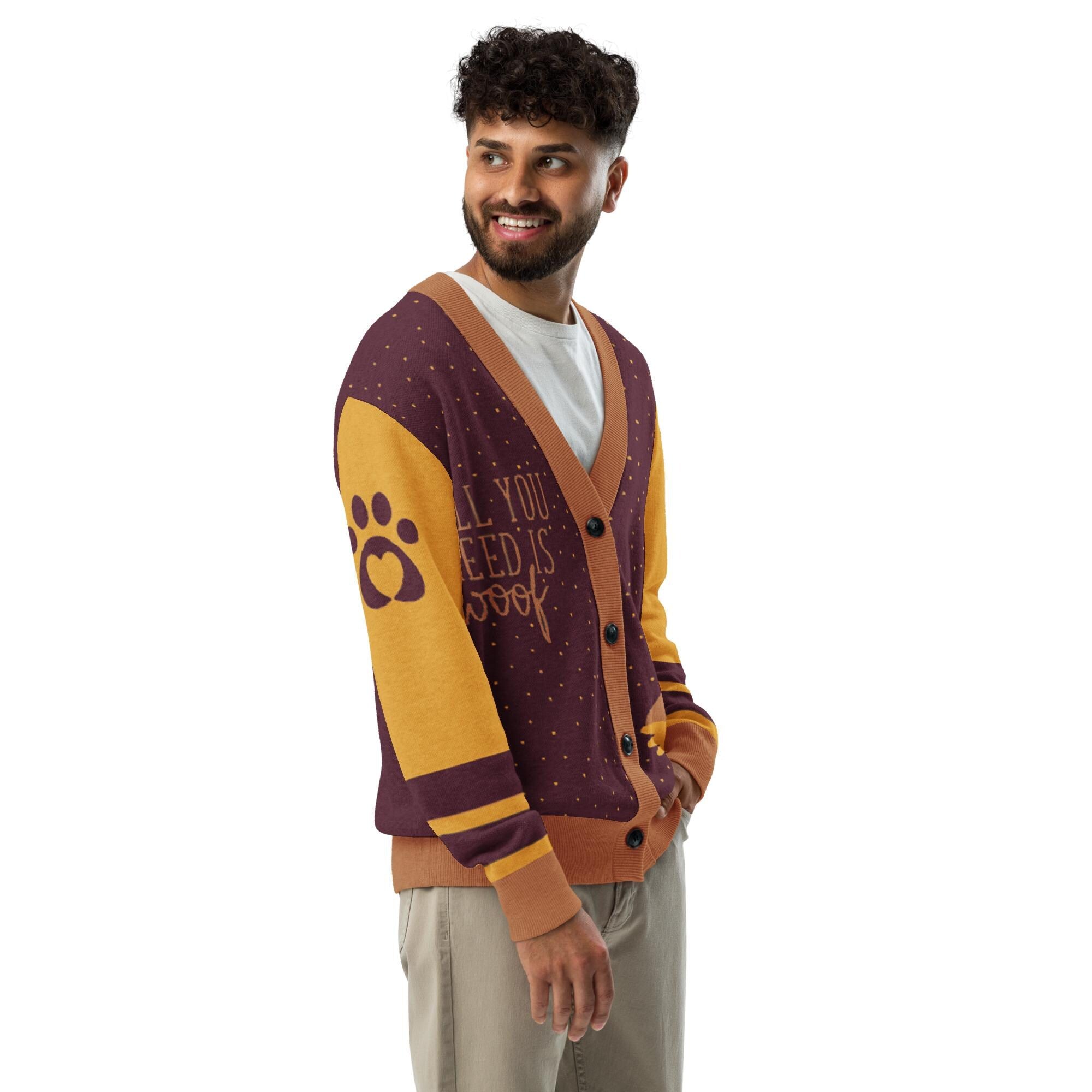 A smiling man wearing a purple and yellow cardigan with a paw print design and the text "All you need is love" printed on it.