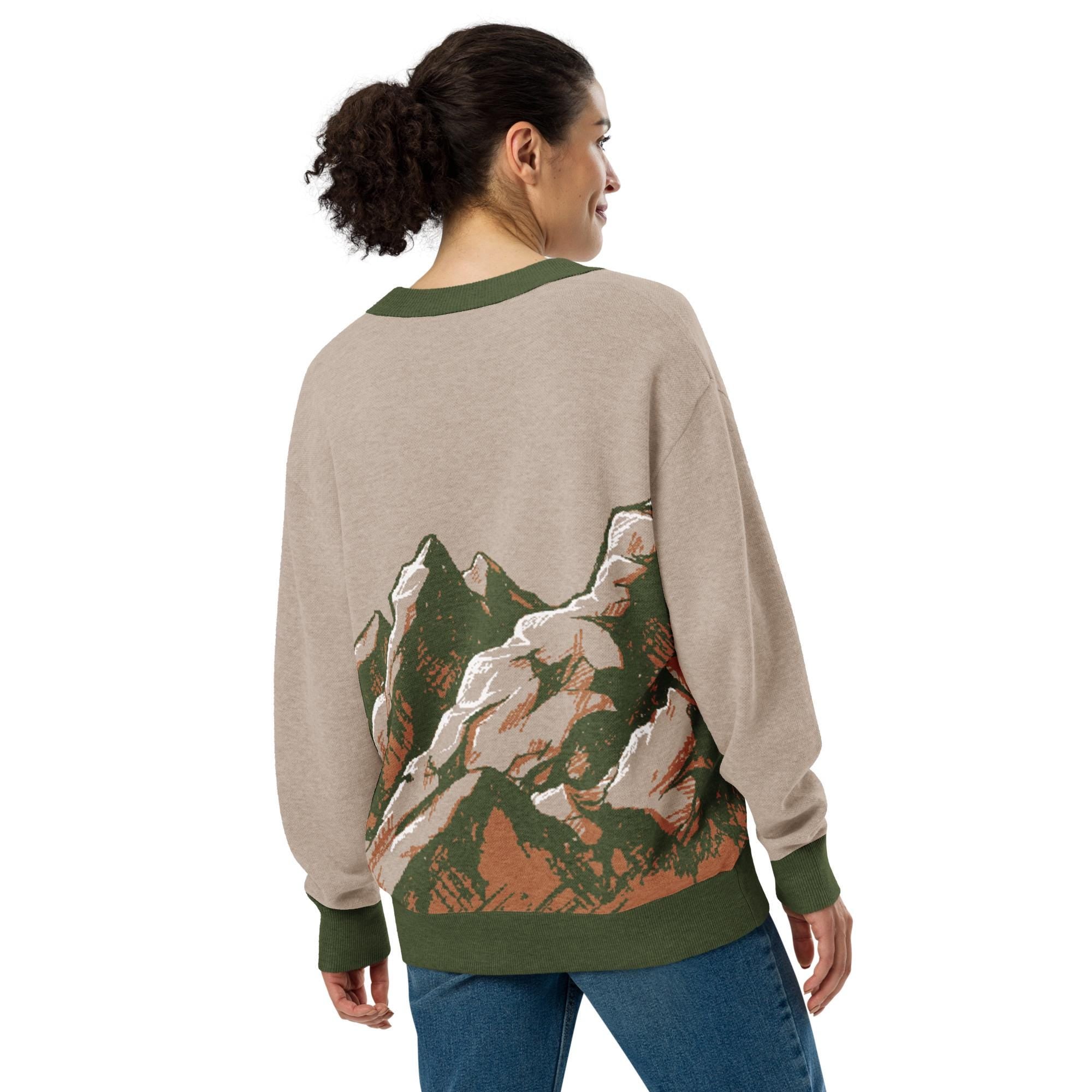 A woman wearing a gray sweater with a mountain landscape design on the back.