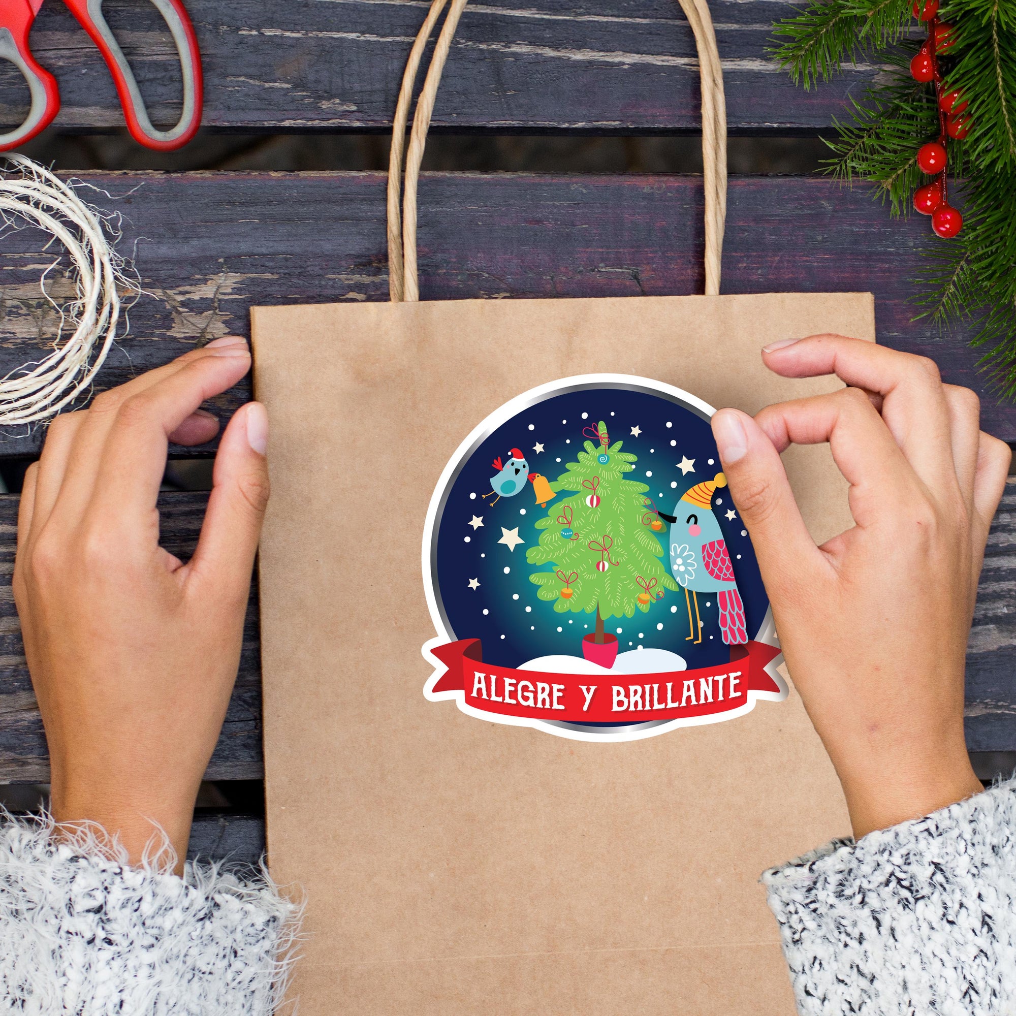 A person&#39;s hands are holding a brown paper bag with a Christmas-themed sticker on it, which features a Christmas tree and birds.