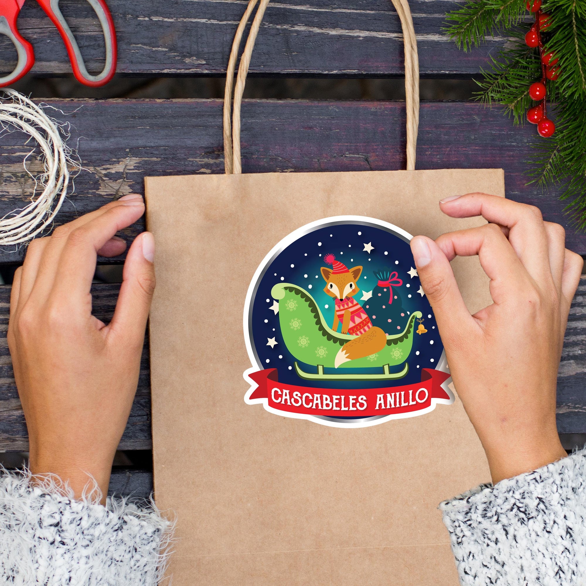 A person&#39;s hands holding a brown paper bag with a sticker featuring a cartoon fox on a sled, surrounded by stars and a red ribbon.