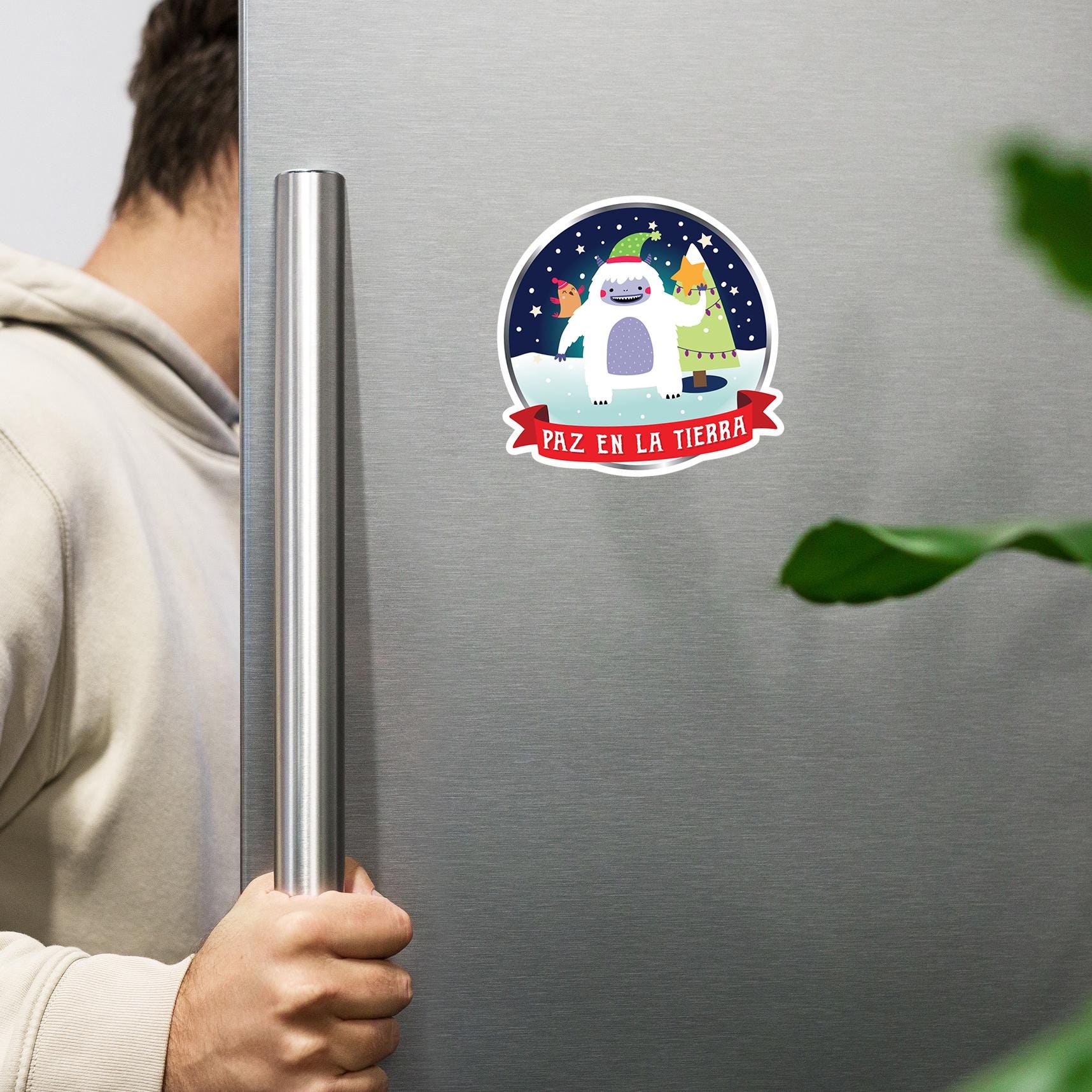 A person is holding a refrigerator handle next to a sticker featuring a cartoon snow monster.