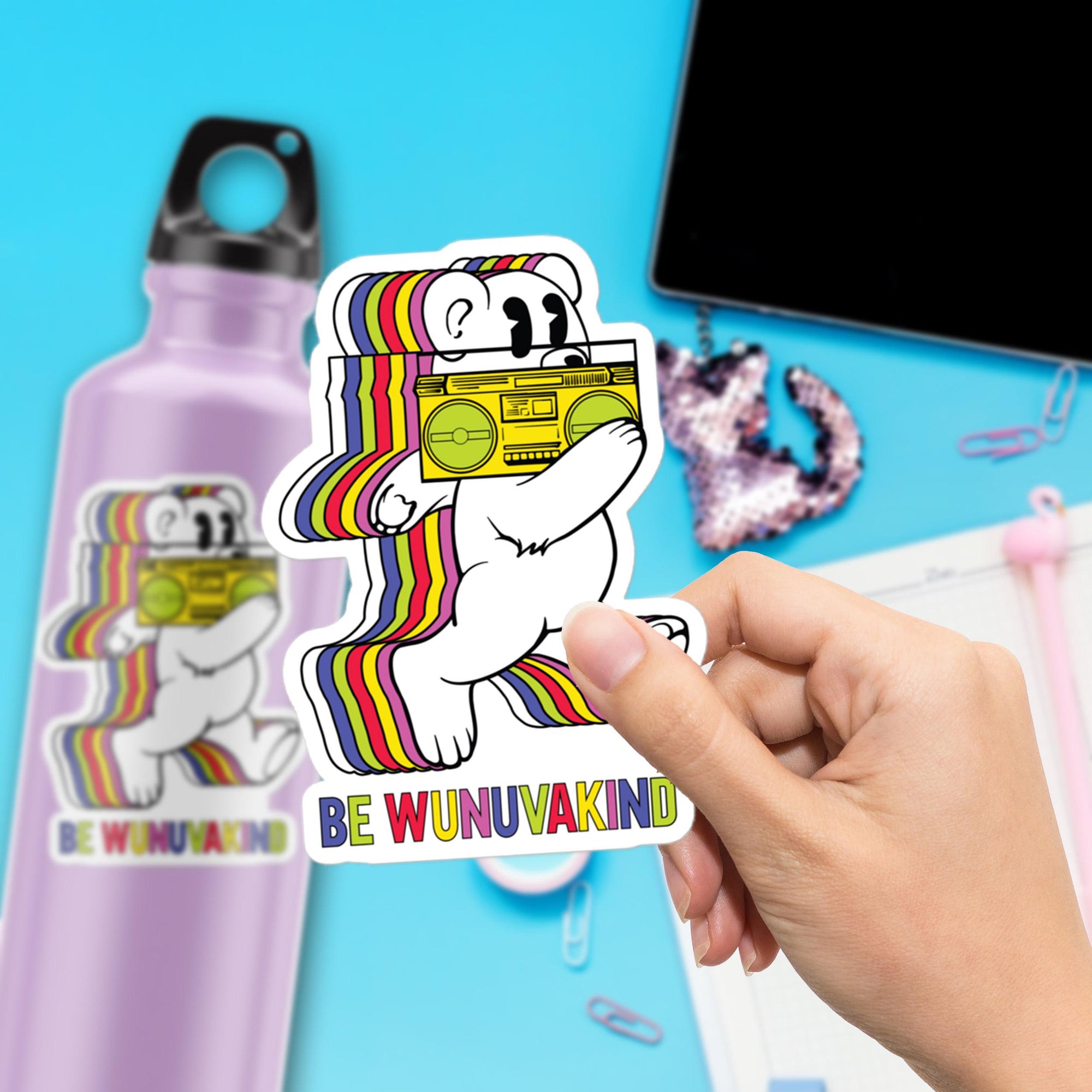A person is holding a sticker with a cartoon bear holding a boombox, with the text "BE WUNUVAKIND" on it.