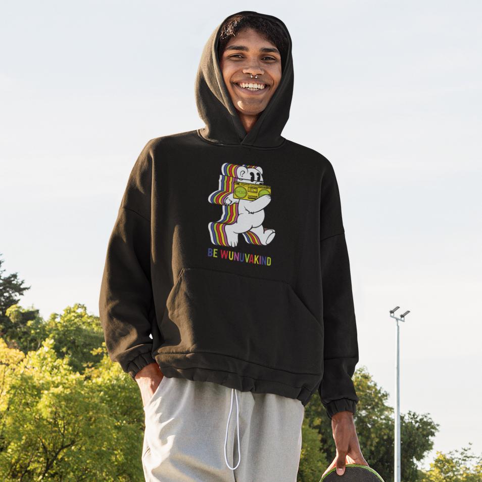 A smiling young man wearing a black hoodie with a colorful graphic of a bear holding a sign that says "Be WUNIKKIND".