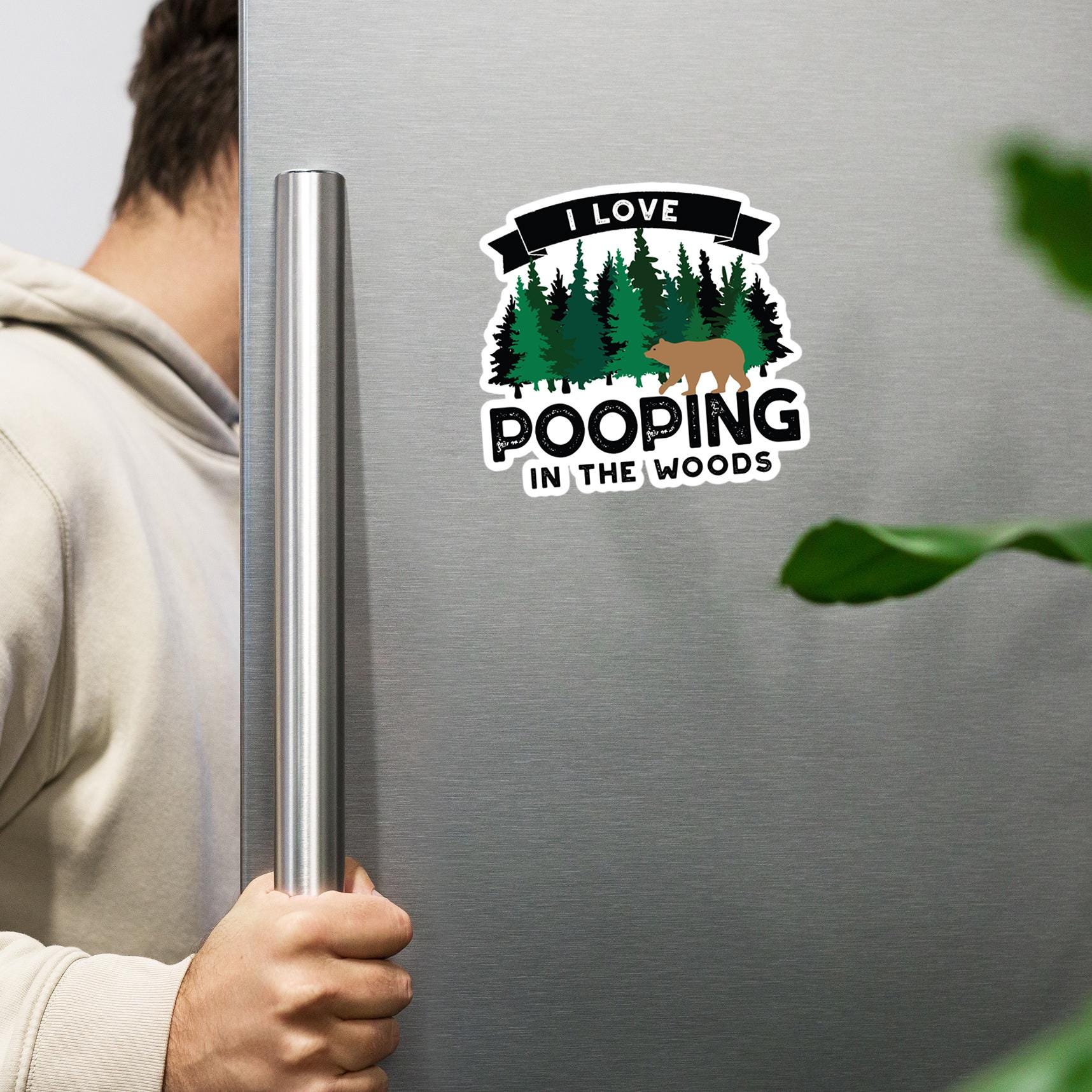 A person is holding a refrigerator handle next to a sticker that says "I LOVE POOPING IN THE WOODS".
