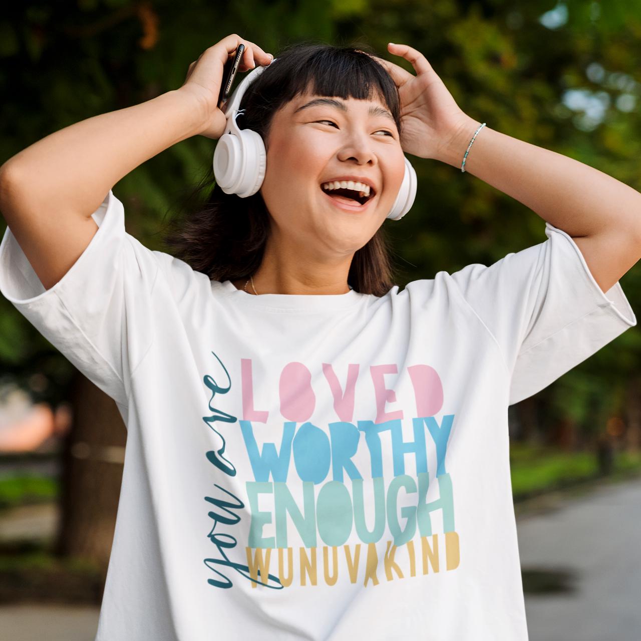 A woman wearing a white t-shirt with a colorful graphic and smiling while listening to headphones.