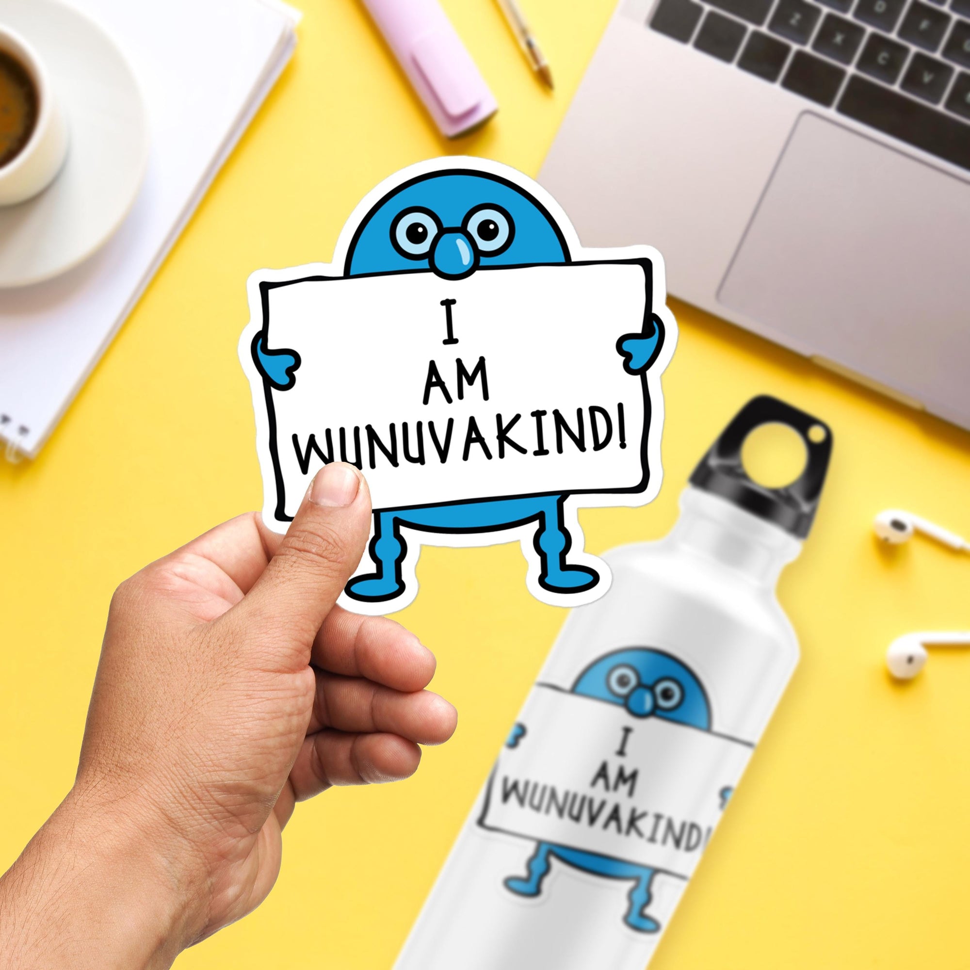 A person's hand holding a sticker with a cartoon character and text, along with a water bottle and other office supplies on a yellow background.