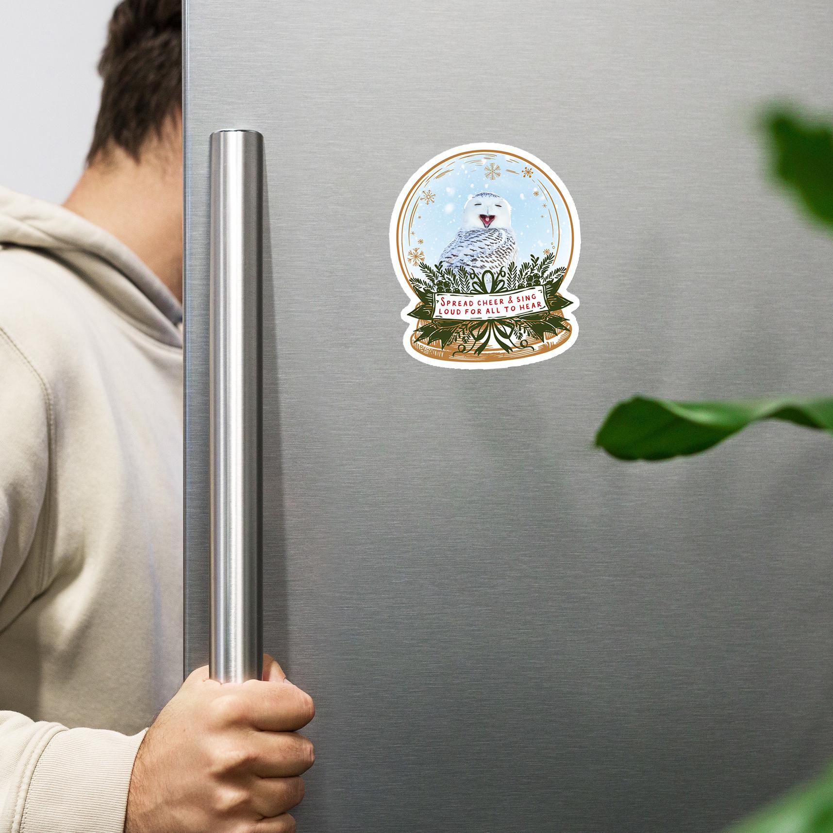 A person is holding a silver refrigerator handle, with a sticker featuring an owl on the door.