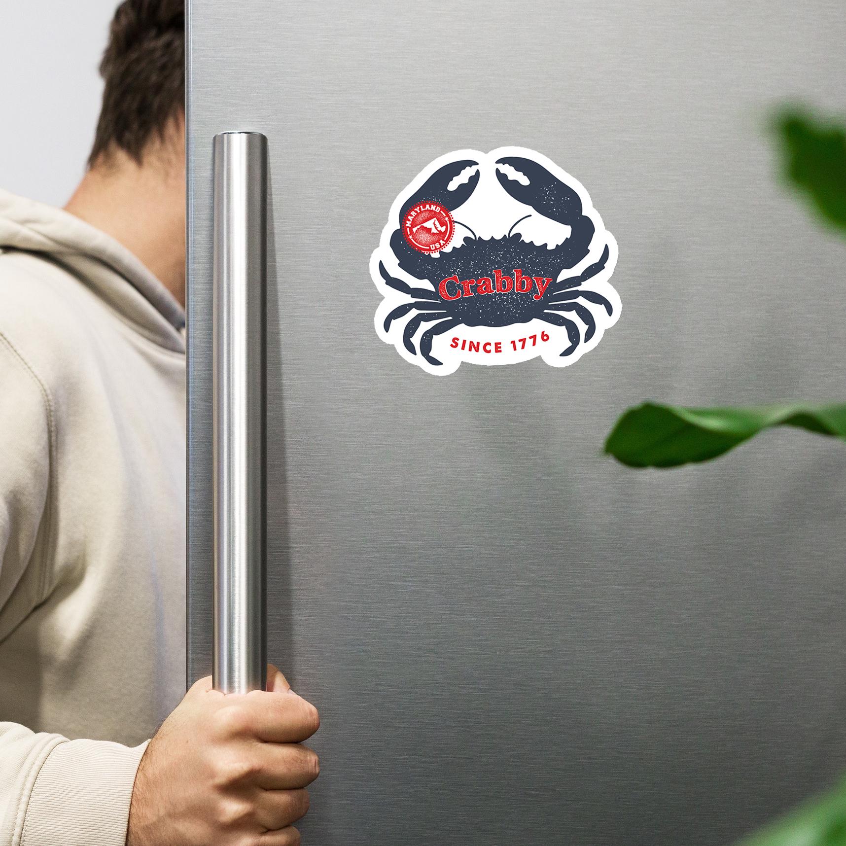 A person is holding a stainless steel refrigerator door with a sticker of a crab on it.