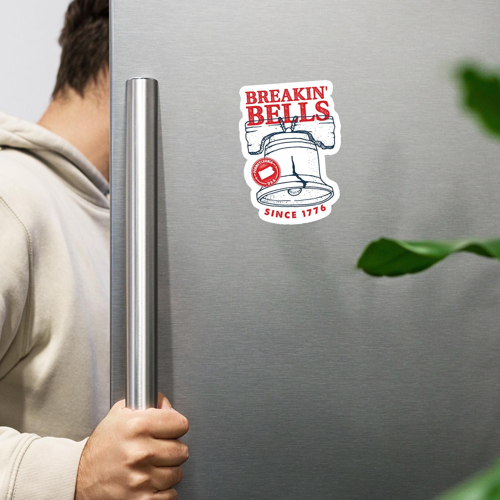 A person is holding a metal handle on a refrigerator door, with a sticker of a bell and the text "BREAKIN' BELLS" on the door.