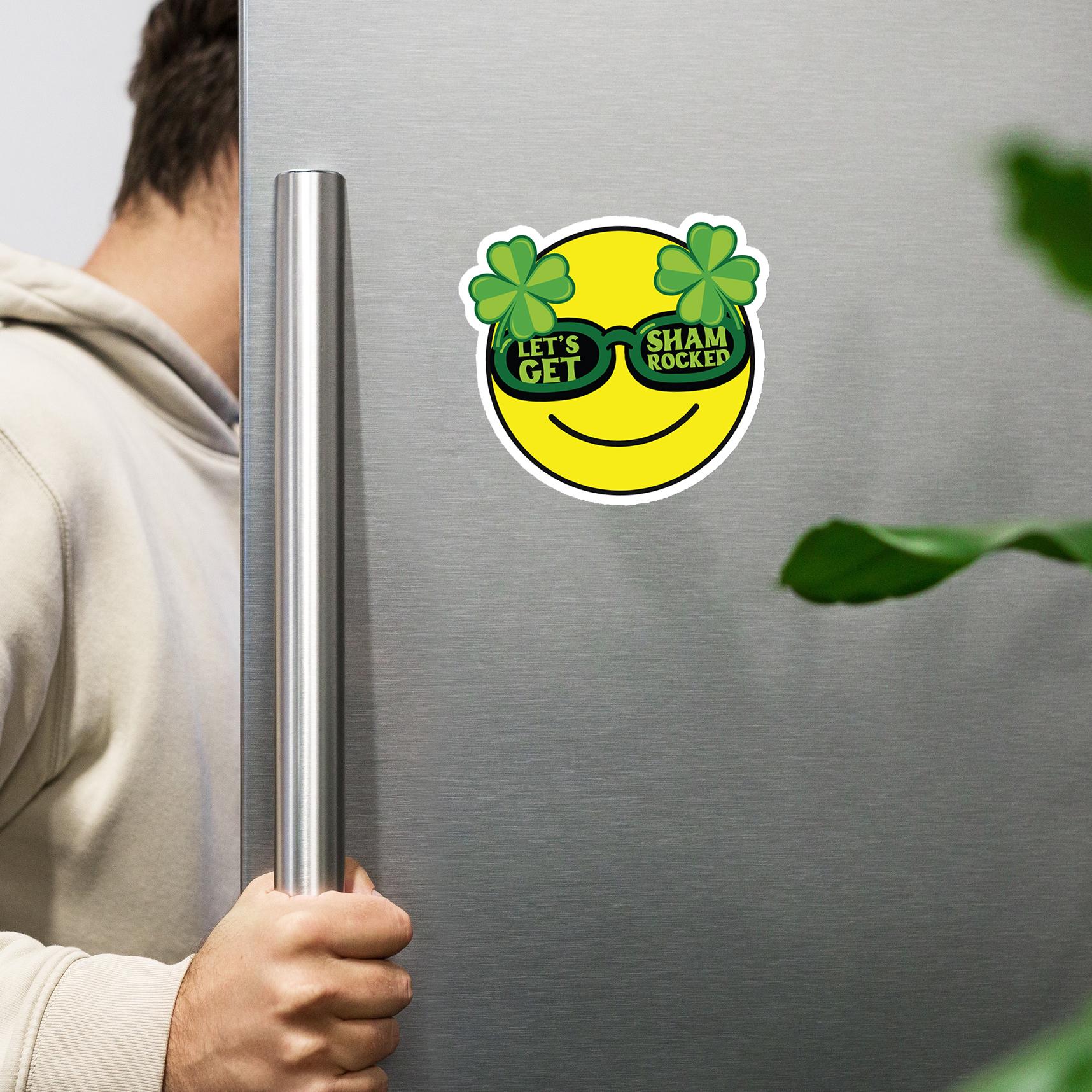A person is holding a refrigerator handle next to a sticker with a smiling yellow face and shamrock glasses.