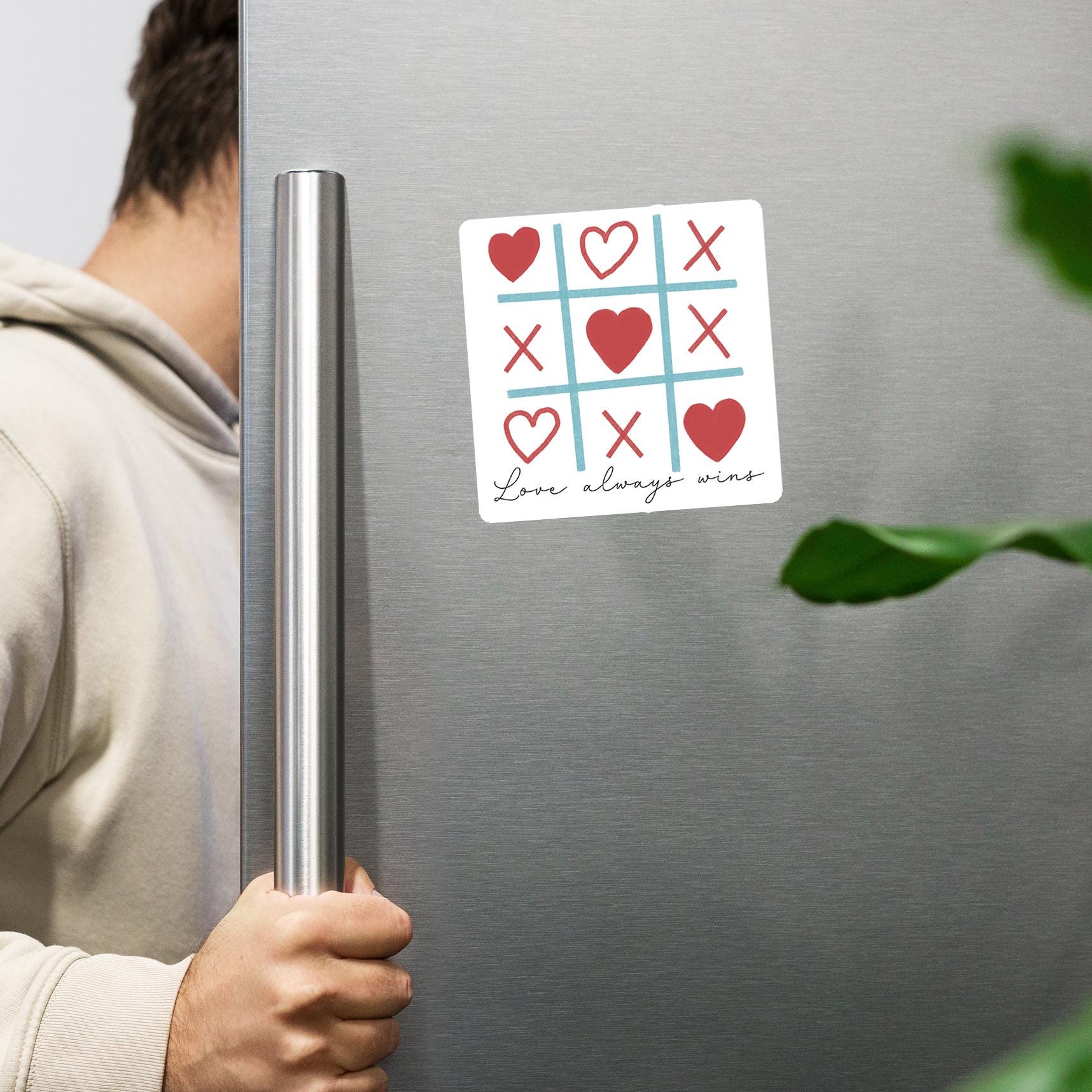 A person is holding a refrigerator door with a magnetic tic-tac-toe magnet on it.